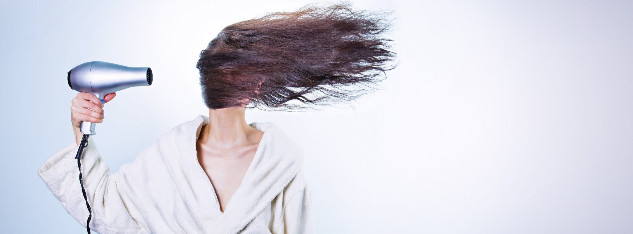 Personne utilisant un sèche-cheveux, symbolisant la mutation dans le secteur de la coiffure.