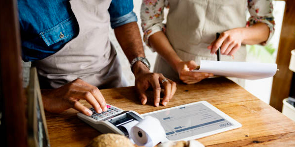 Deux personnes utilisant un pack de caisse enregistreuse avec logiciel, calculant des finances avec une calculatrice et des documents sur une table en bois.